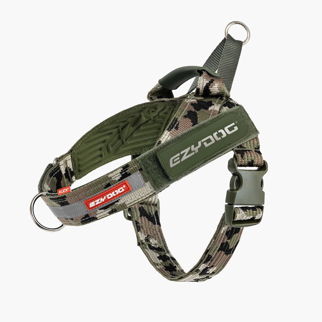 A dog harness in olive green and digital camouflage pattern, featuring a quick-release plastic buckle, metal D-ring, and EzyDog branding.