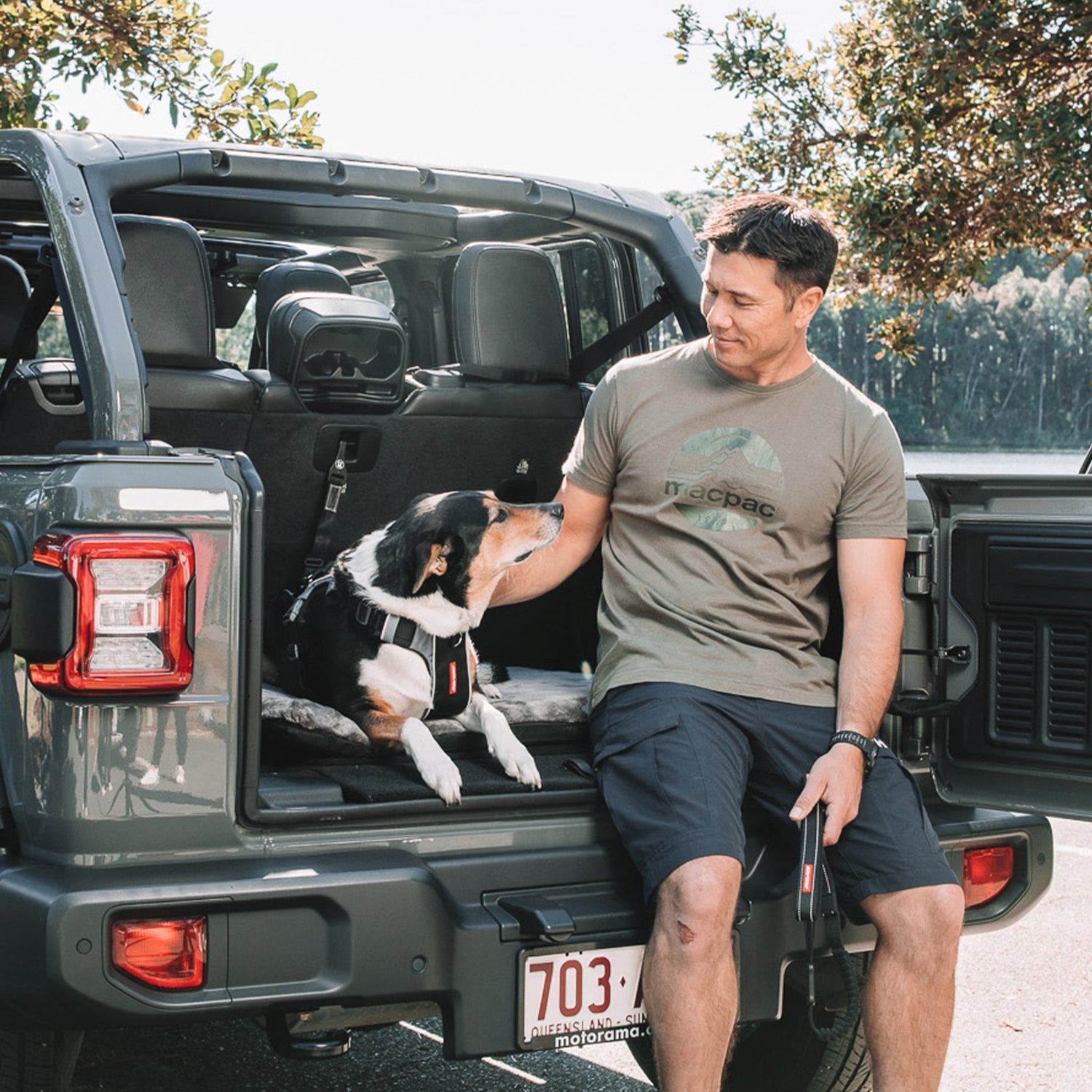 Man with a dog in a car seat cover standing next to an open SUV trunk.