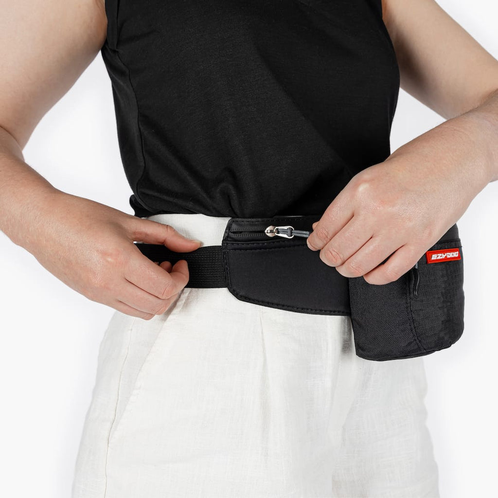 Person wearing a black waist bag with a visible brand logo on a white background