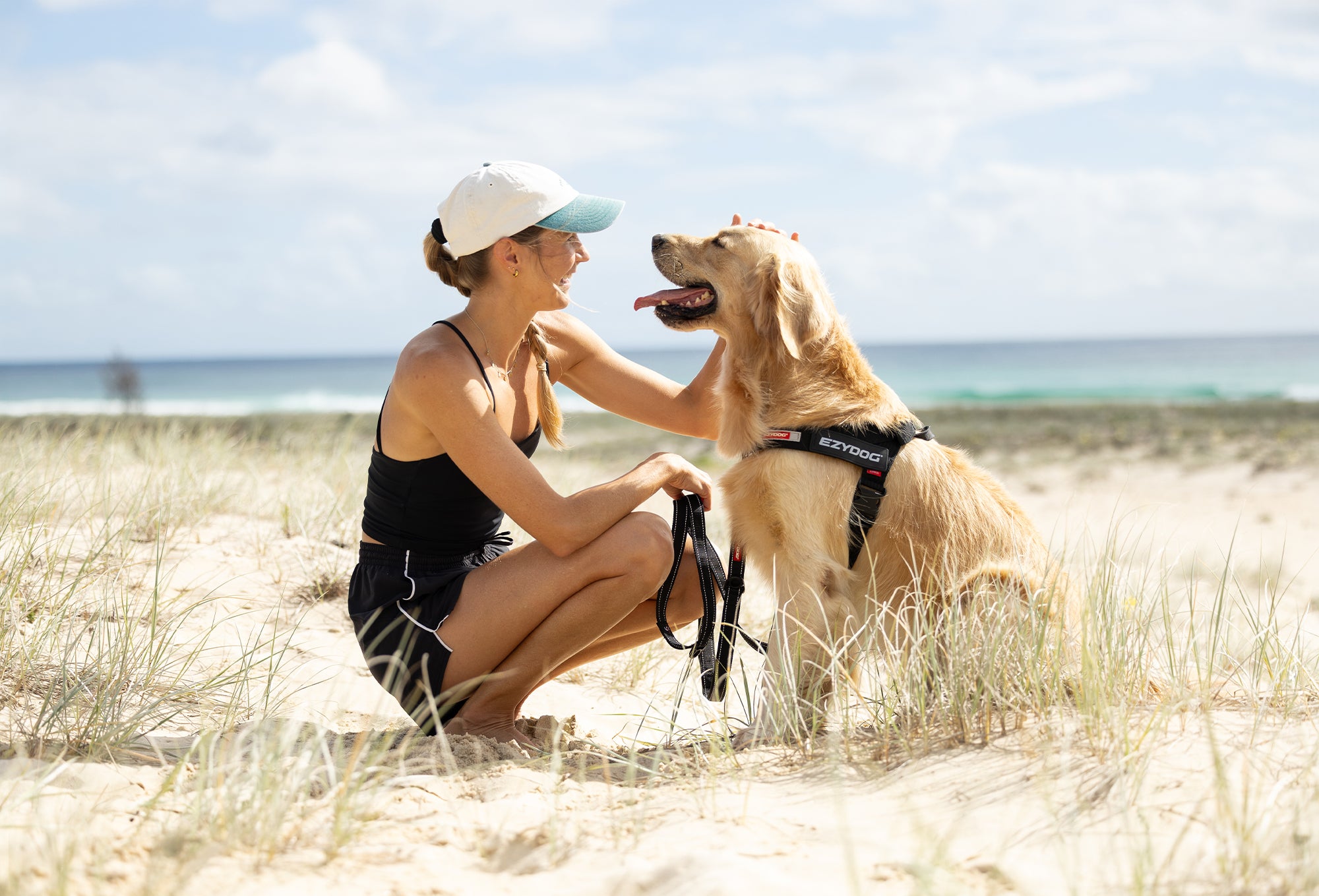 Woman sitting on a sandy beach with a dog, both looking happy