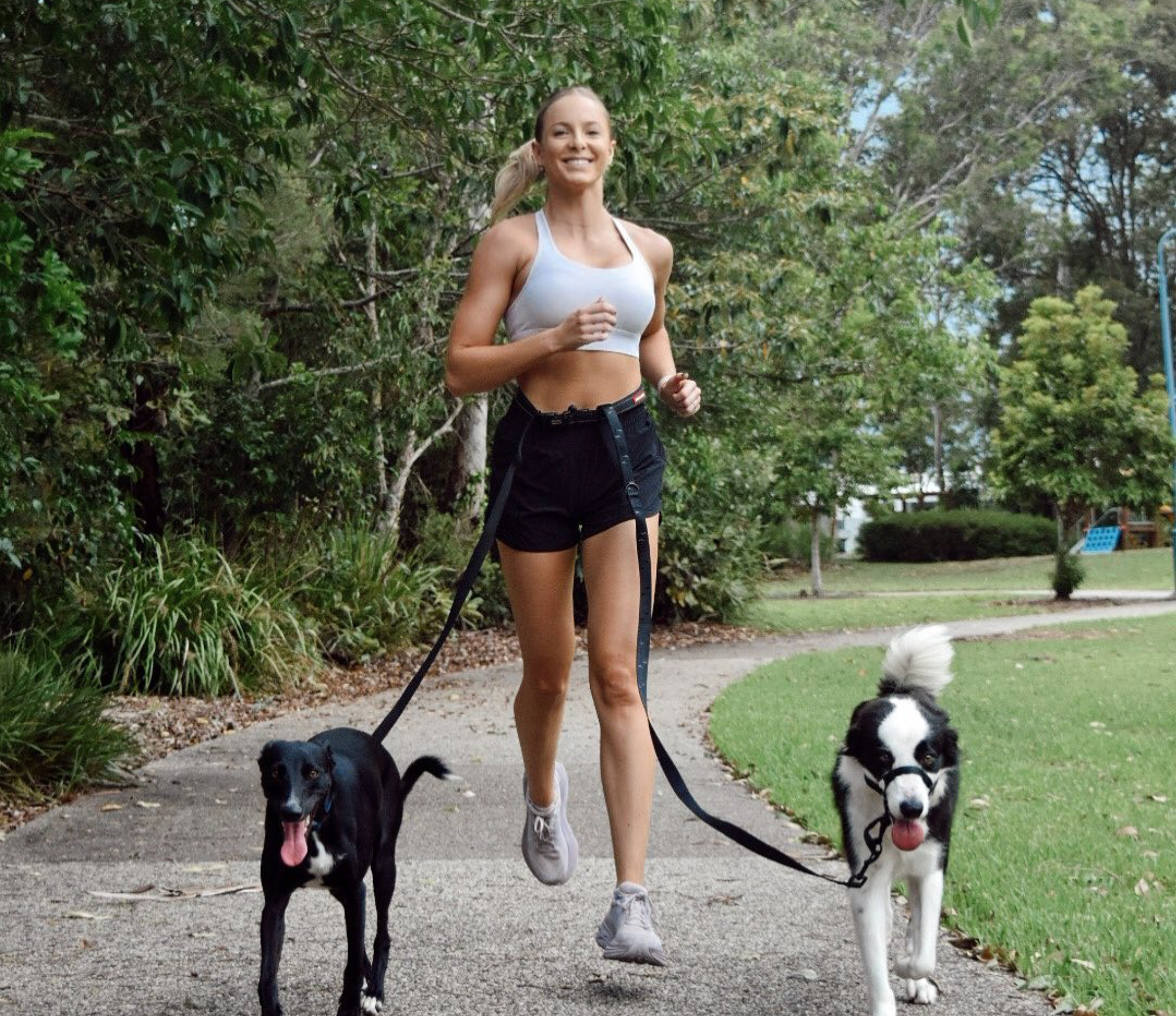 Woman running with two dogs on a path in a park