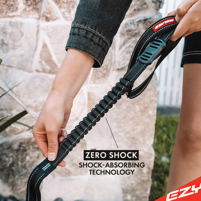 Person holding a black dog leash with shock-absorbing technology against a stone wall background.